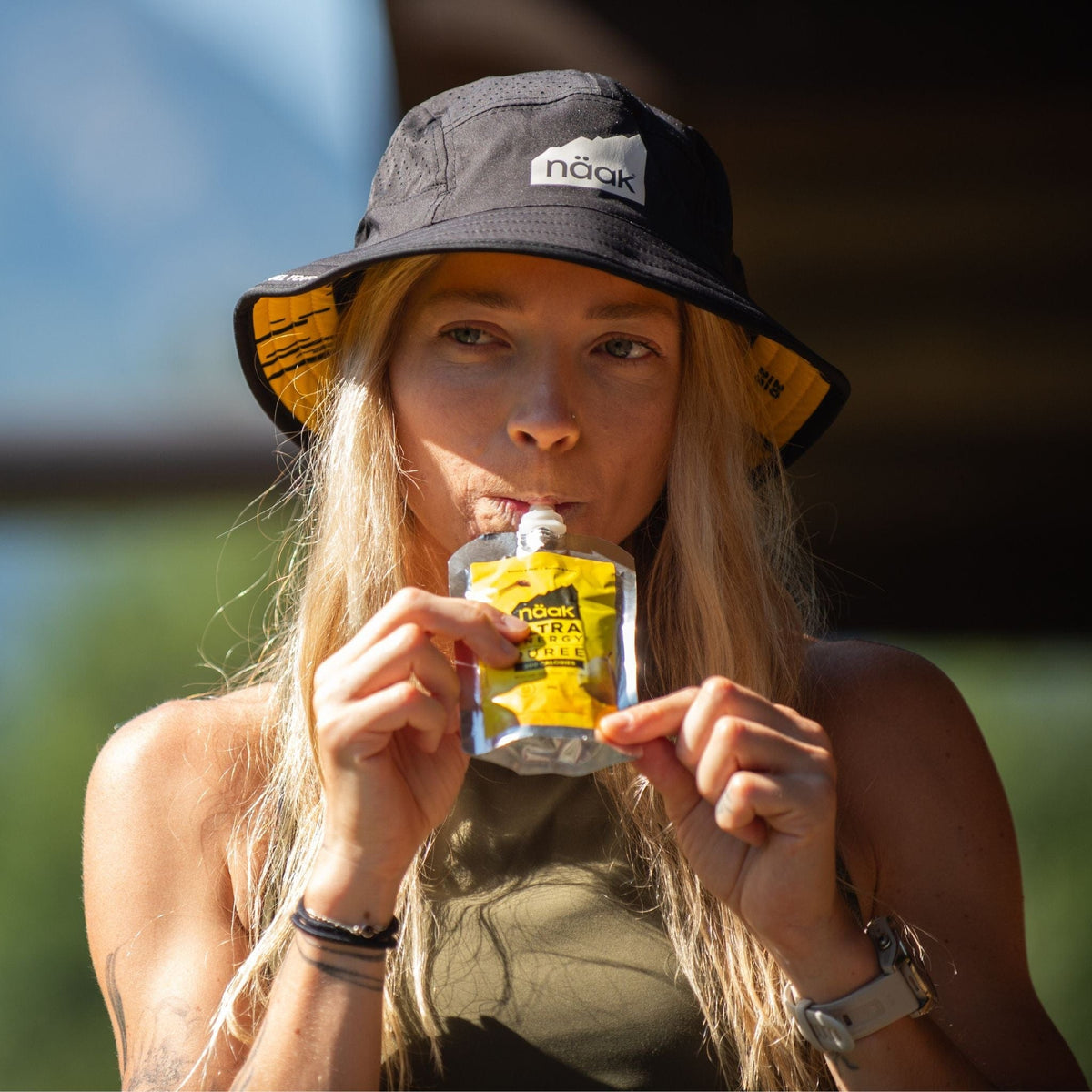 Jazmine Lowther eating a Näak Ultra Energy Puree Banana Pear, wearing a naak bucket hat